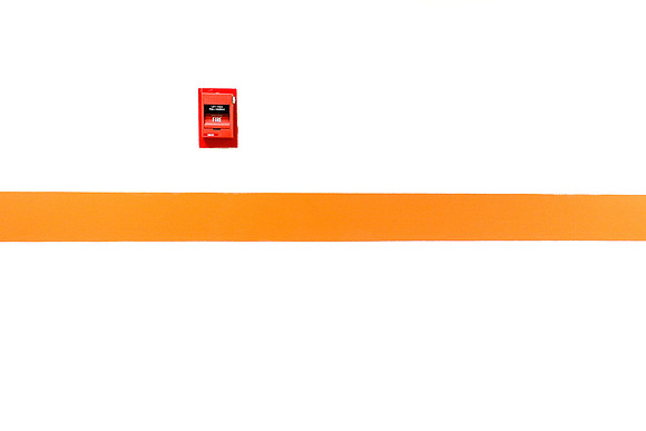 Red Fire Alarm on White Wall with Orange Stripe